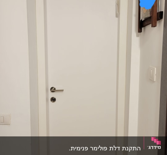דלת לבנה עם ידית כסופה במסגרת קיר לבן